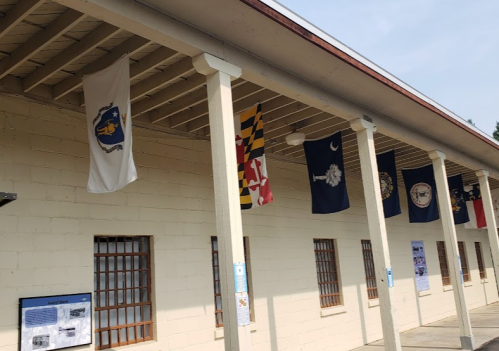 A building exterior with several flags hanging from the roof, featuring various state and military insignias.