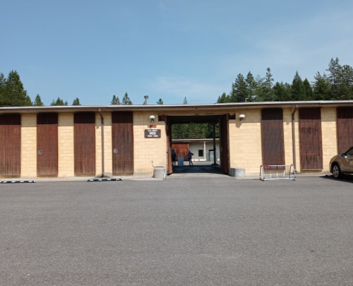 A large building with wooden slatted doors, surrounded by trees, and a parking area in front.
