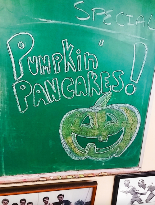 Chalkboard sign featuring "Pumpkin Pancakes!" with a smiling pumpkin illustration.