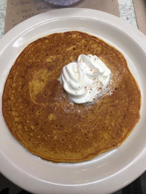 A large pancake topped with a dollop of whipped cream and a sprinkle of cinnamon on a white plate.