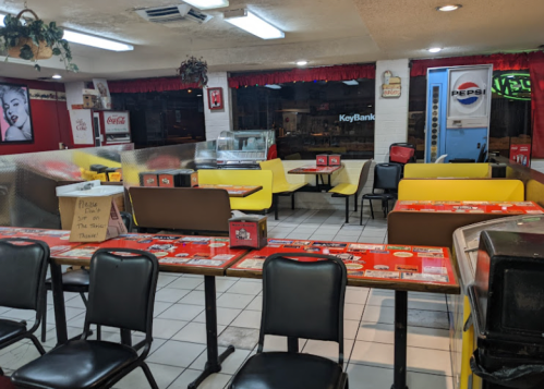 A retro diner interior with yellow booths, black chairs, and tables, featuring vintage decor and a soda machine.