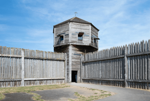 A wooden watchtower surrounded by a tall wooden fence under a clear blue sky.