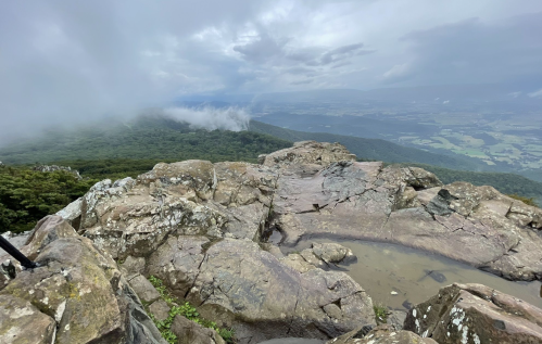 A rocky mountain summit with a misty landscape and clouds in the distance, showcasing a serene natural view.