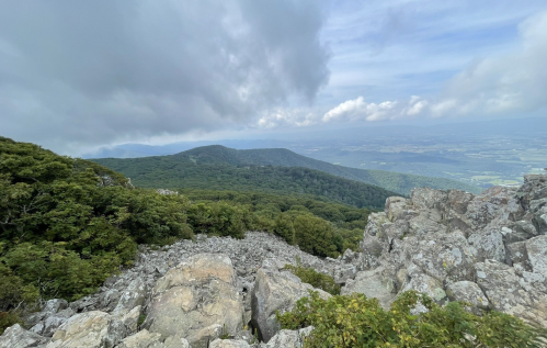 A rocky landscape with lush green hills under a cloudy sky, showcasing a scenic mountain view.