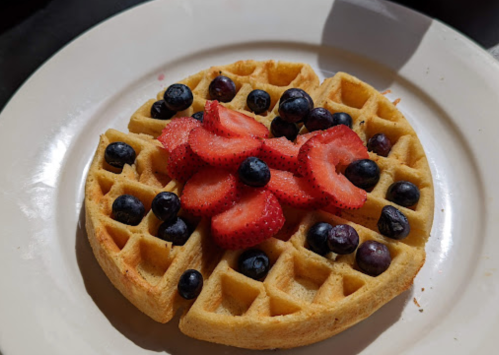 A golden waffle topped with fresh strawberries and blueberries on a white plate.