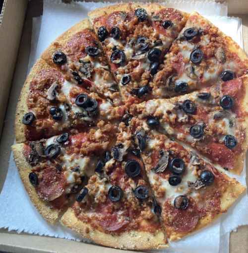 A pizza topped with pepperoni, sausage, black olives, and mushrooms, cut into slices in a pizza box.
