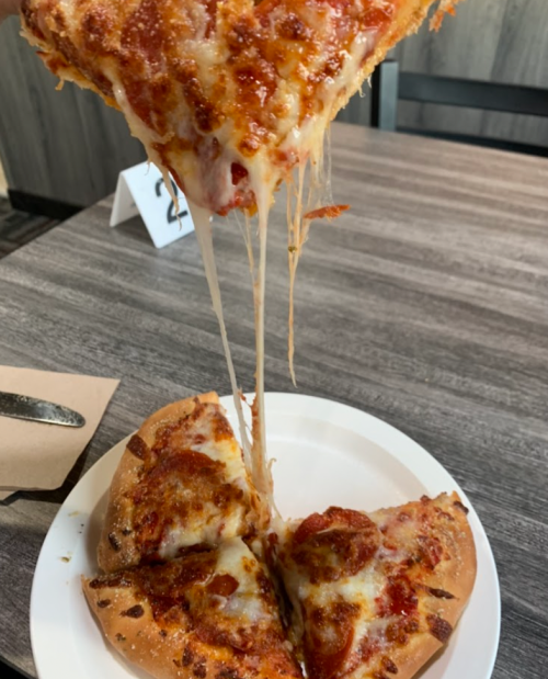 A slice of cheesy pepperoni pizza being lifted, with gooey cheese stretching from the pie on a white plate.