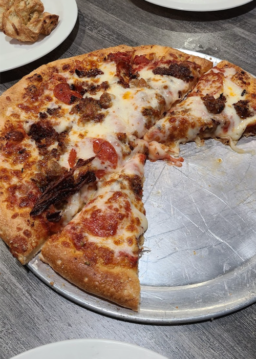 A partially eaten pizza on a metal tray, topped with pepperoni and melted cheese.