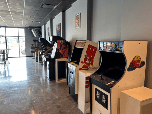 A row of vintage arcade machines in a modern gaming space with a polished floor and minimalistic decor.