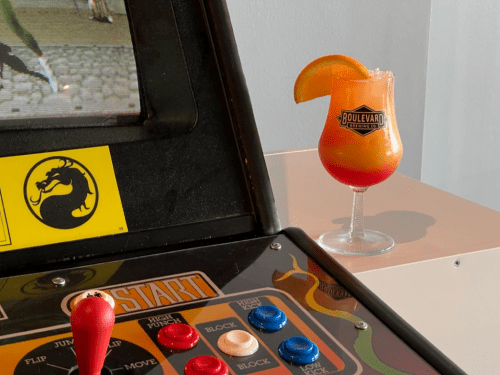 A close-up of a retro arcade game with a colorful cocktail beside it, featuring an orange slice garnish.