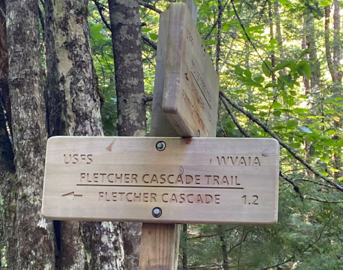 Wooden trail sign indicating "Fletcher Cascade Trail" and "Fletcher Cascade" with a distance of 1.2 miles.