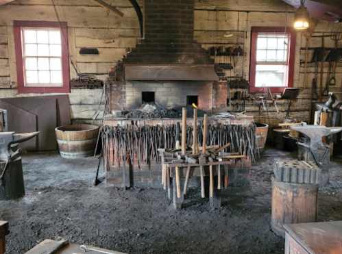A historic blacksmith shop with a large forge, tools, and wooden barrels in a rustic setting.