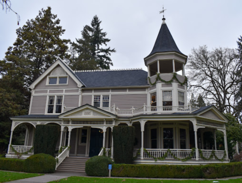 Victorian-style house with a turret, intricate woodwork, and lush greenery, built in 1886.