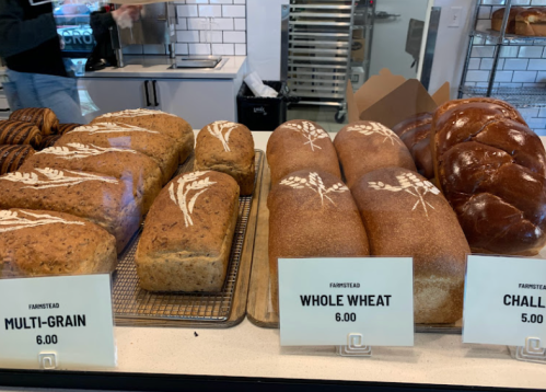 Loaves of multi-grain, whole wheat, and challah bread displayed in a bakery case with prices.