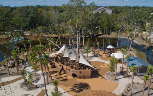 Aerial view of a playground with unique structures, surrounded by trees and a water feature.