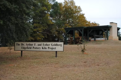 Sign for the Dr. Arthur F. and Esther Goldberg Edgefield Pottery Kiln Project, with a shelter and trees in the background.