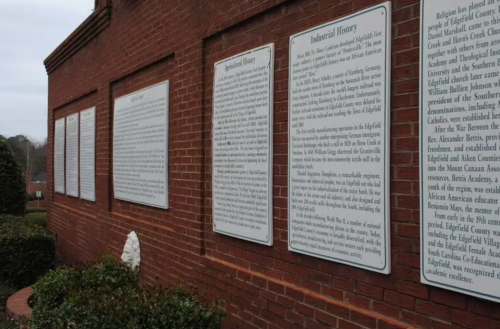 A brick wall displaying several historical plaques detailing local agricultural and industrial history.