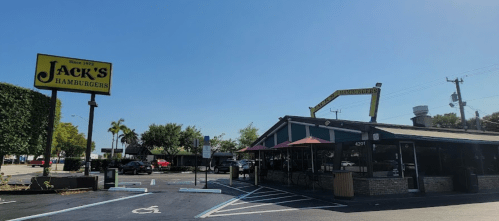 Exterior of Jack's Hamburgers restaurant, featuring a sign and outdoor seating, under a clear blue sky.