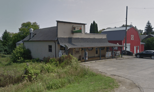 A rustic building with a sign reading "Frosty Inn," surrounded by greenery and a red barn in the background.