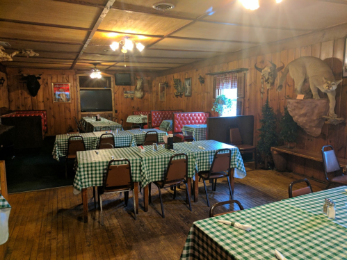 Cozy restaurant interior with wooden walls, checkered tablecloths, and mounted animal heads on display.