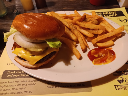 A cheeseburger with lettuce, onion, and fries on a plate, accompanied by a small serving of ketchup.