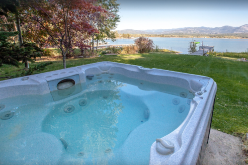 A hot tub overlooking a serene lake and mountains, surrounded by lush greenery and colorful trees.