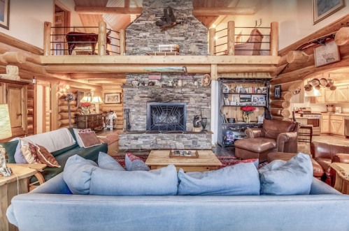 Cozy log cabin interior featuring a stone fireplace, comfortable seating, and rustic decor. Warm and inviting atmosphere.