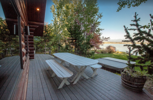 A wooden deck with a picnic table overlooks a serene lake surrounded by trees and greenery.