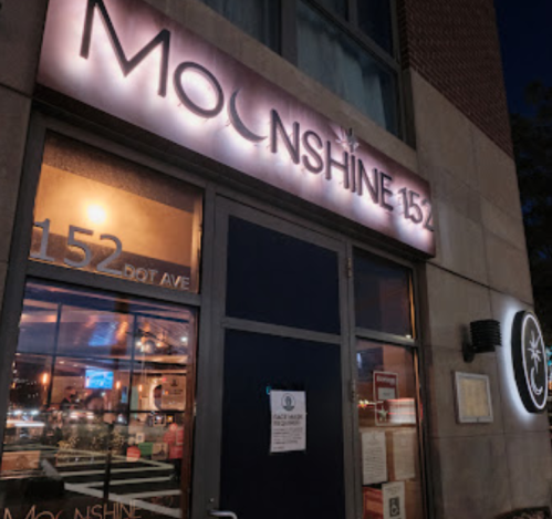 Exterior of Moonshine 152 restaurant, featuring a lit sign and large windows, with a notice on the door.