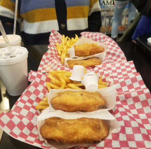 A table with three servings of fried food and fries, served in red and white checkered paper, alongside drinks.