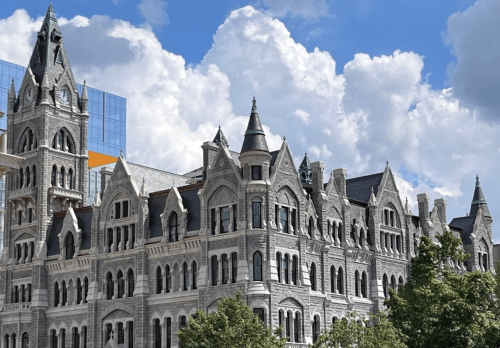 Historic stone building with ornate architecture, featuring towers and spires, set against a blue sky with fluffy clouds.
