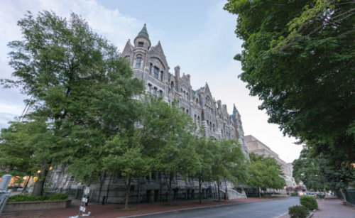 Historic building with intricate architecture, surrounded by lush green trees and a quiet street.