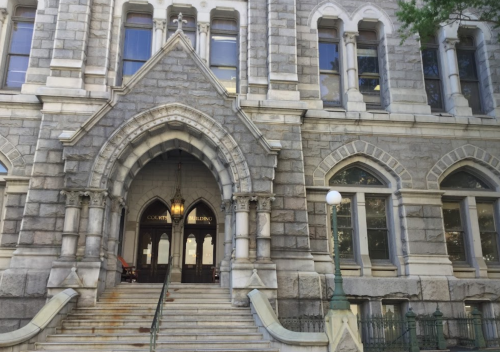 Historic stone building entrance with arched doorway and steps, featuring large windows and decorative architectural details.