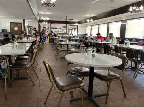 A spacious, mostly empty diner with round tables, chairs, and a few patrons scattered throughout.