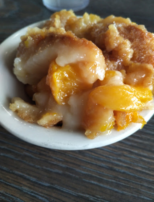 A small bowl of peach cobbler with a golden crust and chunks of peach in a sweet syrup.