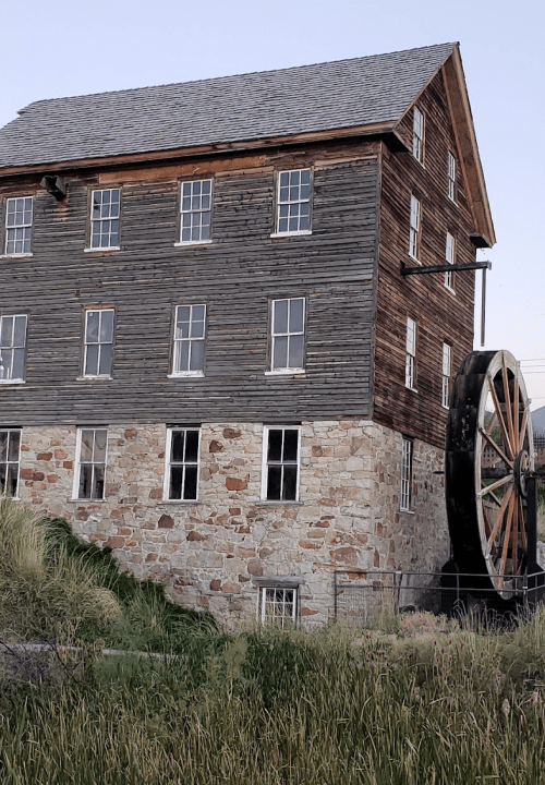 Historic building with a stone base and wooden upper floors, featuring a large water wheel beside it.