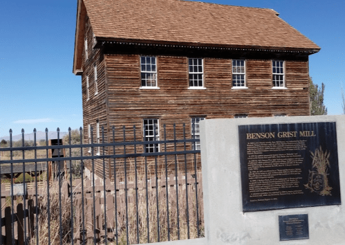 Historic Benson Grist Mill building with wooden exterior, surrounded by a fence and a plaque detailing its history.