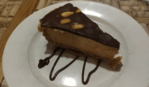A slice of chocolate peanut butter pie on a white plate, drizzled with chocolate sauce and topped with almonds.