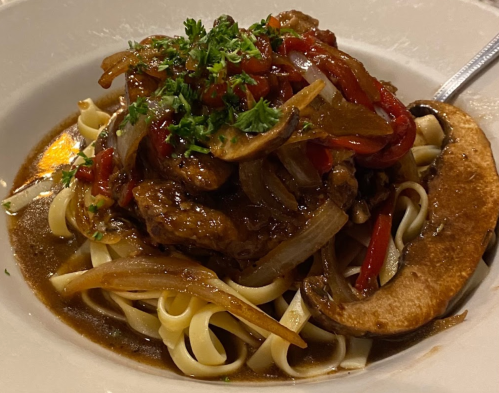 A plate of fettuccine topped with sautéed chicken, bell peppers, onions, and mushrooms, garnished with parsley.