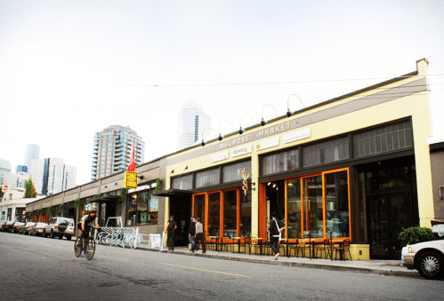 A street view of Melrose Market with people walking and a cyclist passing by, surrounded by urban buildings.