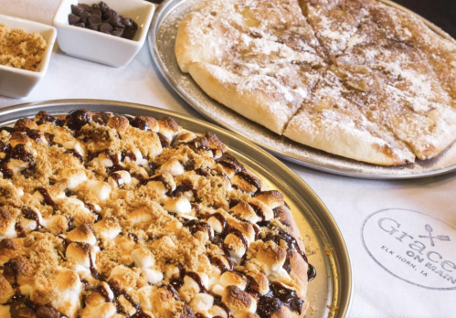 A close-up of two dessert pizzas: one topped with chocolate, marshmallows, and crumbs, the other with powdered sugar.