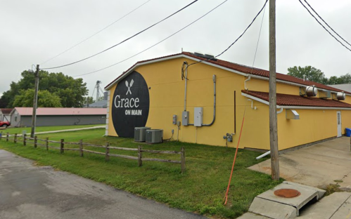 A yellow building with a large black sign reading "Grace on Main," surrounded by utility equipment and power lines.