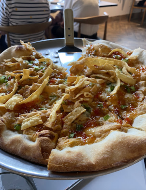 A pizza topped with shredded chicken, green onions, and crispy tortilla strips on a metal serving tray.