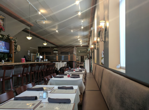 Interior of a restaurant featuring tables with white tablecloths, a bar area, and warm lighting.