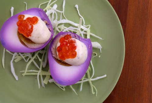 Two purple-hued egg halves topped with cream and red caviar, served on a bed of shredded cabbage.