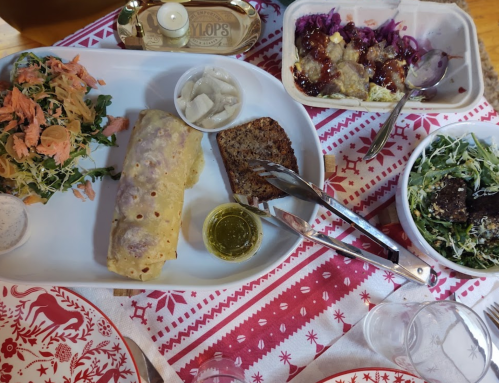A festive table setting with a plate of enchiladas, salad, bread, and a side dish, all on a decorative tablecloth.