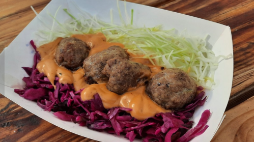 A serving of meatballs on a bed of purple cabbage, topped with a creamy sauce and garnished with shredded lettuce.