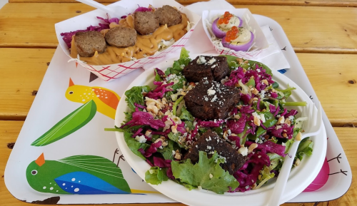 A colorful meal featuring a salad with greens, purple cabbage, and dark pieces, alongside meatballs and dessert treats.