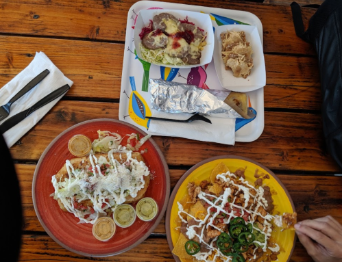 A colorful tray with various Mexican dishes, including tacos, a burrito, and a plate of fried food with toppings.