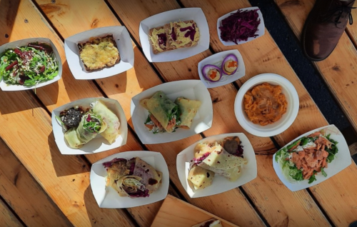 A variety of colorful dishes arranged on a wooden table, including wraps, salads, and small appetizers.